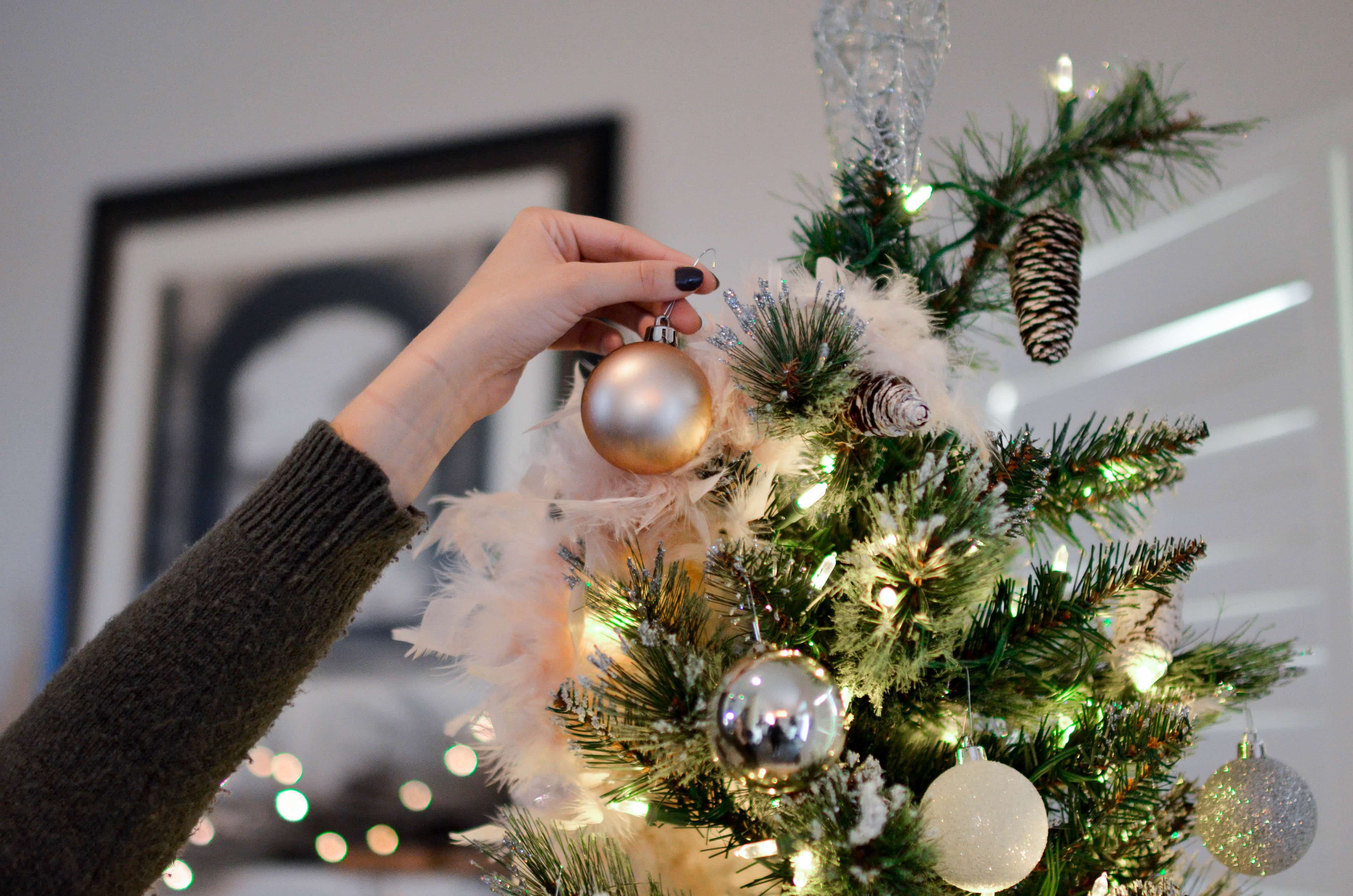 5 Ways to Protect a Christmas Tree from Rodents-Woman's hand hanging a bulb on a tree.
